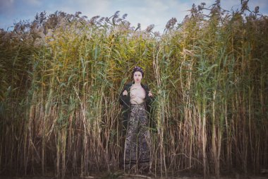 Sonbahar günbatımında nehir kamışlarının arasında üstsüz bir kadın duruyor..