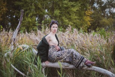 Sonbahar günbatımında nehir kamışlarının arasında üstsüz bir kadın duruyor..