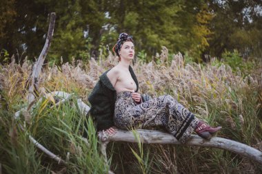 Sonbahar günbatımında nehir kamışlarının arasında üstsüz bir kadın duruyor..