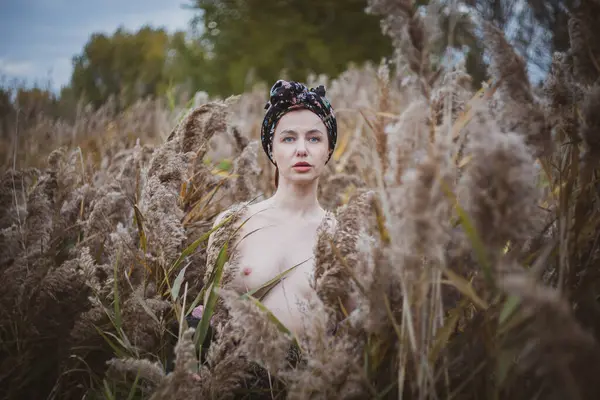 Sonbahar günbatımında nehir kamışlarının arasında üstsüz bir kadın duruyor..