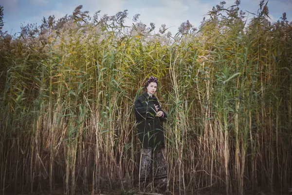 Sonbahar günbatımında nehir kamışlarının arasında üstsüz bir kadın duruyor..