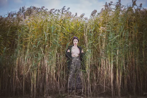 Sonbahar günbatımında nehir kamışlarının arasında üstsüz bir kadın duruyor..