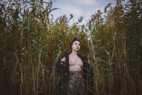 Sonbahar günbatımında nehir kamışlarının arasında üstsüz bir kadın duruyor..