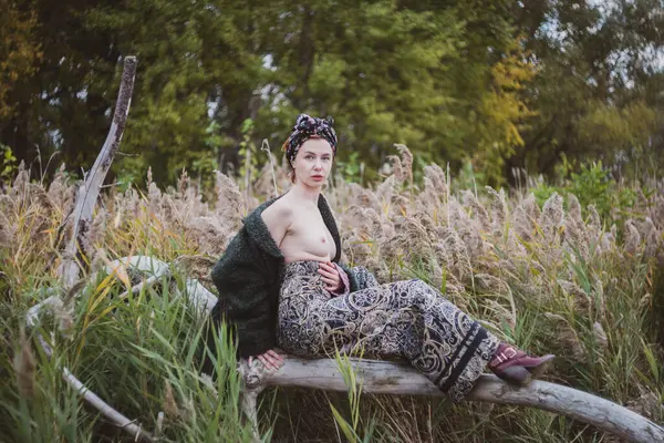 Sonbahar günbatımında nehir kamışlarının arasında üstsüz bir kadın duruyor..