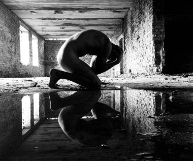 Ham duygusal durgunlukla tuğlalarla çerçevelenmiş çıplak figür..