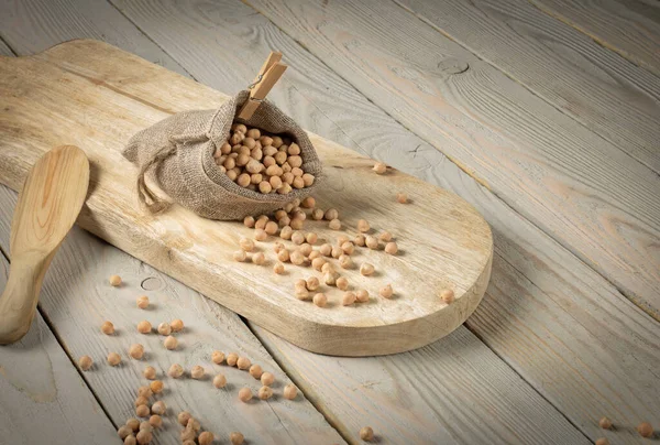 Still life, chickpeas in a bag on a wooden table. Part of the peas scattered on the table, rustic style