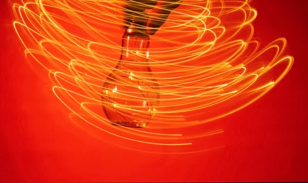 Christmas accessory-garland of LED light bulbs in a glass flask on a red abstract background. The hand with the flask makes oscillatory movements, leaving a luminous plume in the background