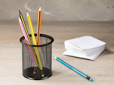 Mesh office container with pencils and a stack of paper for notes on the background of the office table.