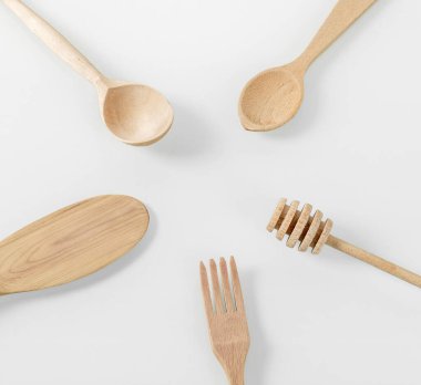 Ahşap mutfak aletleri. Çeşitli ahşap mutfak aletleri daire şeklinde dizilir, merkezde metin için bir yer vardır. Kaşıklar, çatallar, bal çubuğu, beyaz arka planda spatula..