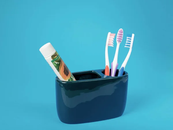 一套三套彩色牙刷 一管环保牙膏 装在蓝色底座的陶瓷容器中 — 图库照片