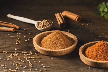 Ahşap mutfak masasında, mantar tabağındaki çeşitli baharatlar. Oregano, karabiber, taco, karanfil, tarçın