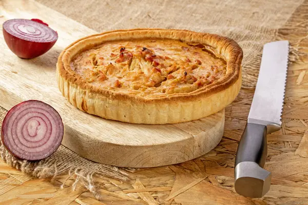 French onion pie with bacon on the kitchen board, cut onion and knife on the kitchen table