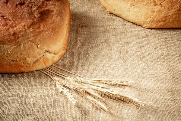 Çuval bezi masa örtüsünde somun ekmek ve bir demet arpa kulağı görünür..