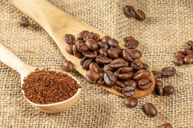 Kahve teması. Kahve çekirdekli iki tahta kaşık ve öğütülmüş kahve granülleri çuval bezi peçetenin üzerinde yatıyor.