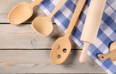 Çeşitli ahşap mutfak aksesuarları ve dokulu doğal ahşap zemine karşı düzgünce katlanmış bir havlu. Sıcak ve dünyevi tonlar mutfak sahnesine sıcak bir hava katıyor..