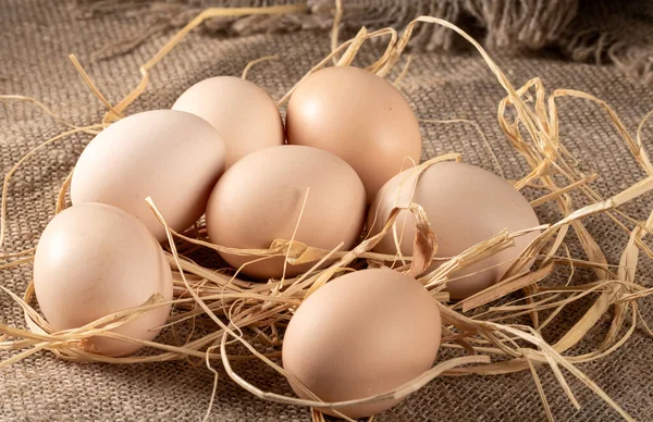 A close-up of fresh chicken eggs arranged on a rough-hewn peasant table with a burlap tablecloth, highlighting the beauty of natural, farm-fresh produce.