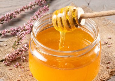 Altın kenevir balı ve kırsal bir masanın üstünde duran ahşap bal kaplamalı cam kavanozun yakın plan çekimi. Bu görüntü konsepti balın doğal tatlılığını iletir..