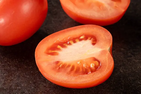 A close-up of a vibrant, freshly sliced tomato, with water droplets glistening on its surface, displayed on a sleek and elegant black background, perfect for culinary or health-related concepts.
