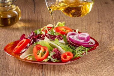 Renkli ve taze bir sebze salatasının üzerine altın zeytinyağı döken cam sürahinin yakın plan çekimi sağlıklı ve iştah açıcı bir yemek yaratıyor..