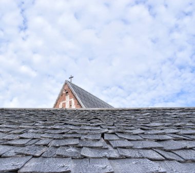 Tipik bir Norveç köy evi çatısı ahşap levhalardan yapılmış ve arkasında Lüteriyen kilisesi haçı var.