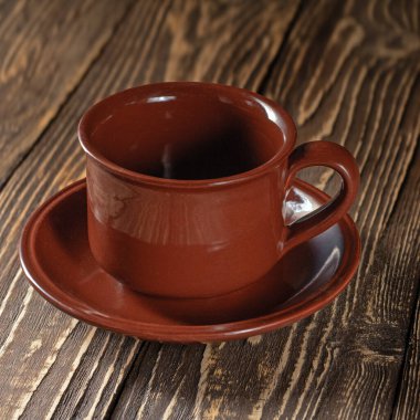 Boş bir kahve fincanı ve fincan tabağının yer aldığı basit ama çarpıcı bir fotoğraf. Tahta bir masa arkasına kurulmuş bu kompozisyon minimalizmi vurgular ve barışçıl kahve anlarını davet eder.