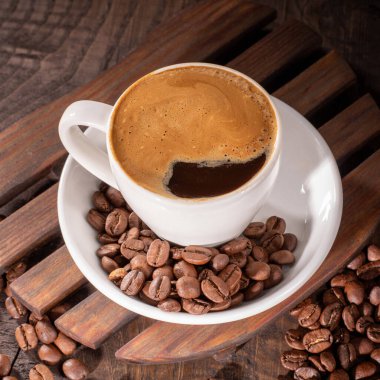 Bu cezbedici görüntü, kadife köpükle kaplanmış ve kahvenin rahatlatıcı ve hoşgörülü dünyasını vurgulayan zengin kahve çekirdekleri tarafından çevrelenmiş lezzetli bir fincan kahveyi içeriyor..