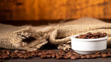 Bu resim, kahve çekirdekleri ile dolu bir fincanı mutfak masasına koyuyor, kahve çekirdekleri dökülüyor. Sıcak tonlar ve kırsal ortam kahve severler için mükemmel bir ortam yaratıyor..