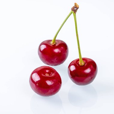 Parlak kırmızı renklerini ve parlak görünümlerini sergileyen, el değmemiş beyaz arka planda duran olgun kirazların güzel bir kenar görüntüsü. Yiyeceklerle ilgili görüntüler için ideal.