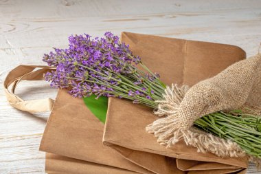 Bu büyüleyici görüntü, kağıt çevre dostu bir alışveriş çantasının üzerinde zarif bir şekilde duran canlı bir lavanta buketi yakalar. Sürdürülebilirlik, doğa ve alışveriş temaları için ideal.