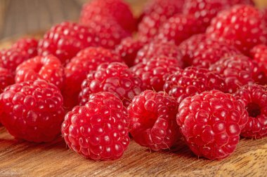 Bu yakın plan görüntü canlı kırmızı rengi ve olgun ahududu dokusunu kırsal ahşap bir masaya serpiştirir. Tazelik ve sağlıklı beslenme için mükemmel..