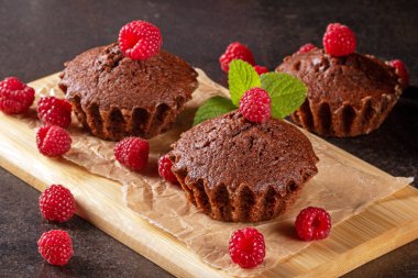 Pürüzsüz, siyah bir mutfak masasında sergilenmiş taze pişmiş keklerin ve canlı ahududuların zevkli manzarasının tadını çıkarın. Her fırıncı için davetkar bir manzara.