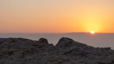 View of the rising sun over the mountains of Jordan from the ruins of the fortress wall of the fortress of Masada - is a fortress built by Herod the Great on a cliff-top off the coast of the Dead Sea, in southern Israel