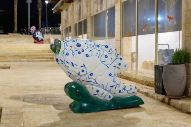 Eilat, Israel, December 13, 2022 : Night view of a decoratively painted abstract stone fish sculpture on the embankment, in the center of Eilat city in southern Israel