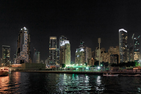 Dubai, United Arab Emirates, March 16, 2023 : Night view from the promenade of Dubai Marina with illuminated skyscrapers, a water channel, yachts and ships in Dubai city, United Arab Emirates