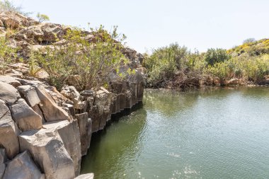 Kuzey İsrail 'deki Yehudia Ulusal Doğal Parkı' ndaki ağaçların ve çalıların olduğu altıgen kayaların çerçevelediği küçük bir göl.