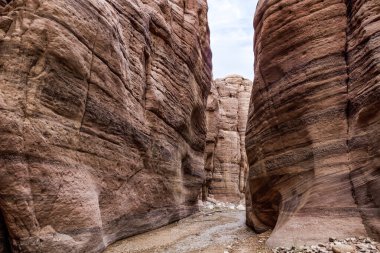 A small shallow stream flows between high rocks with beautiful natural patterns on their walls along walking trail in Wadi Numeira gorge in Jordan