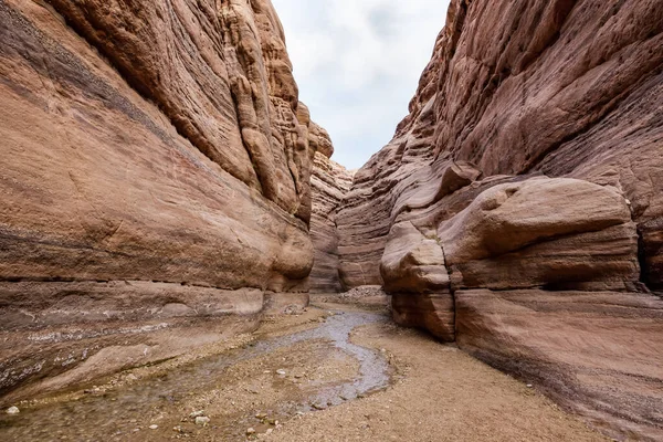 A shallow stream flows between rocks painted with intricate natural patterns at beginning of the Wadi Numeira hiking trail in Jordan