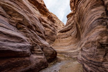 Ürdün 'deki Wadi Numeira yürüyüş yolunun başlangıcında sığ bir derenin her iki yakasındaki yüksek dağların güzel desenleri.