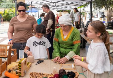 Petah Tikva, İsrail, 18 Nisan 2025: İsrail 'in Petah Tikva kentindeki bahar şövalyeleri festivalinde eğitmen ziyaretçilere eski dokuma tezgahında nasıl çalışacaklarını gösteriyor