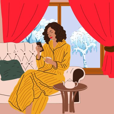 Kız pencerenin yanındaki kanepede kış manzaralı oturuyor. Kar mevsimi. Hygge konsepti. Sıcak sonbahar günleri