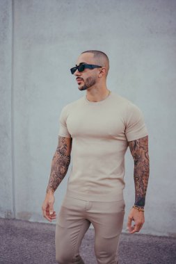 Sakallı ve güneş gözlüklü yakışıklı genç adam şık kıyafetler giyiyor.