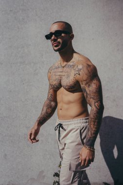 Güneş gözlüğü takan ve dışarıda poz veren yakışıklı genç kaslı adam.