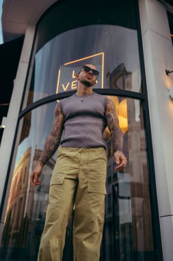 Güneş gözlüklü genç yakışıklı adam moda kıyafetler içinde poz veriyor.