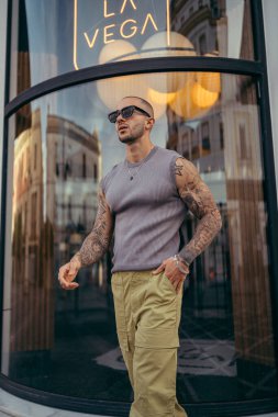 Şık güneş gözlüklü ve şapkalı yakışıklı adam şehrin sokaklarında poz veriyor. Şehrin sokaklarında poz veren şık bir adam. Modaya uygun bir adam
