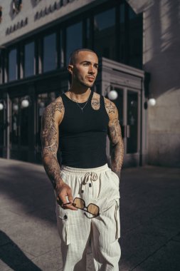 Beyaz tişörtlü, kulaklıklı, genç, yakışıklı, sakallı adam şehirde poz veriyor.