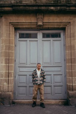 Genç adam bina kapısının yanında duruyor..