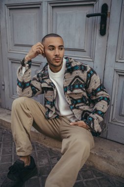 Gri bir duvarda oturan rastalı genç yakışıklı adam..
