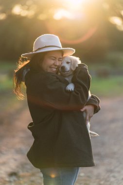 Genç bir kadın doğada sevimli küçük bir köpeğe sarılıyor.