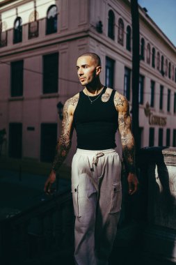 Beyaz gömlekli genç adam şehir caddesinde poz veriyor.