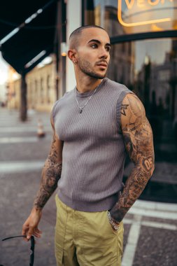Dövmeleri olan şık bir genç adam şehirde poz veriyor.